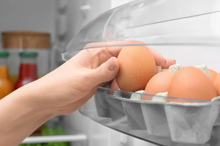 como organizar alimentos en la nevera: mano cogiendo huevos en la nevera